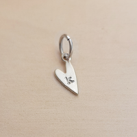 Silver heart-shaped pendant with a letter 'K' on a beige background