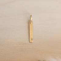 silver pendant with engraved letter 'N' on a beige background