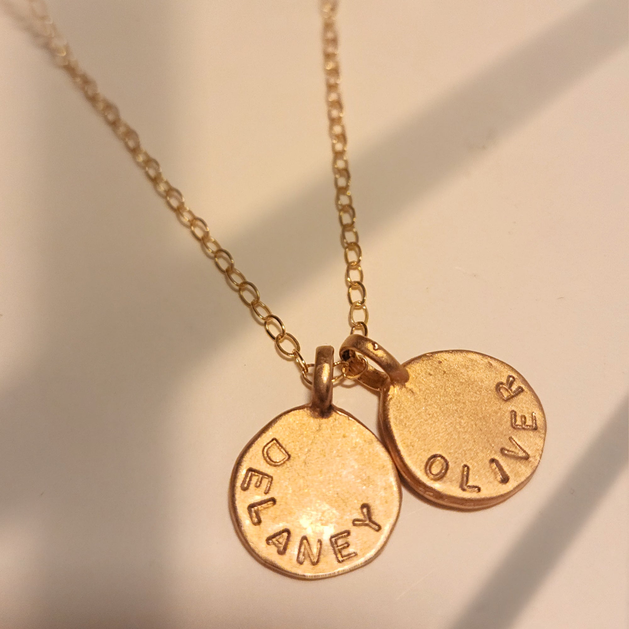Gold necklace with two round pendants engraved with names on a soft background