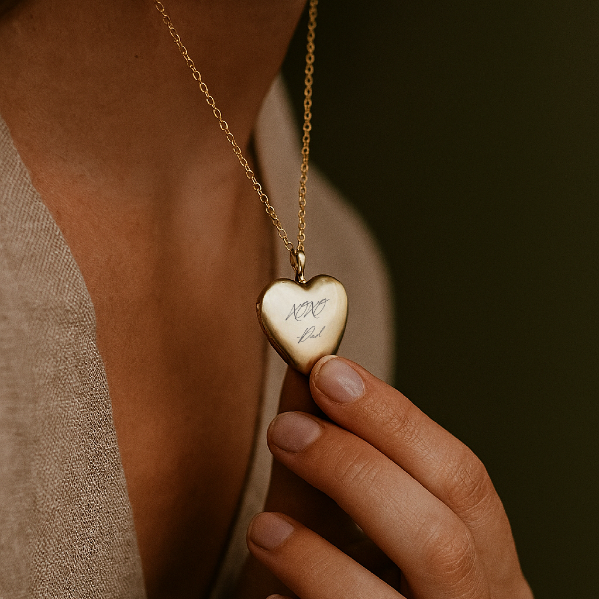 Heart-shaped gold pendant necklace held by a hand against a dark background