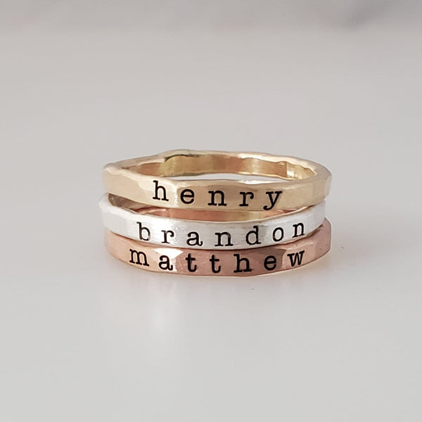 Three stacked rings made of different metals, with the names 'henry', 'brandon', and 'matthew' engraved on them, displayed on a white surface.