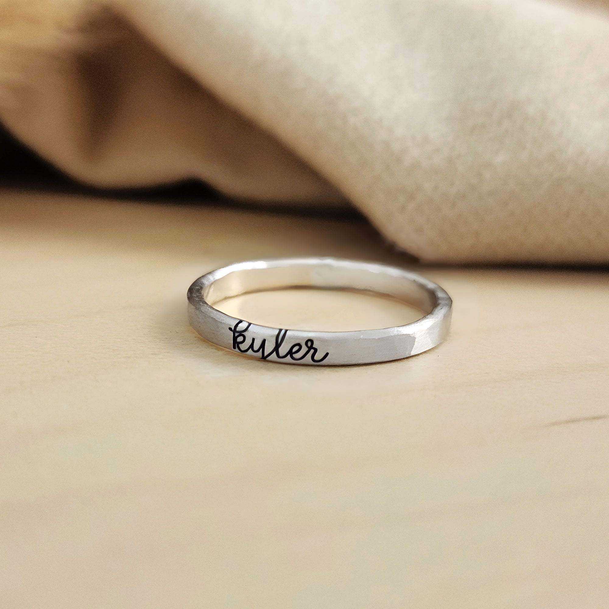 A gold-colored thin ring with cursive script engraving on a white background.