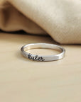 A gold-colored thin ring with cursive script engraving on a white background.