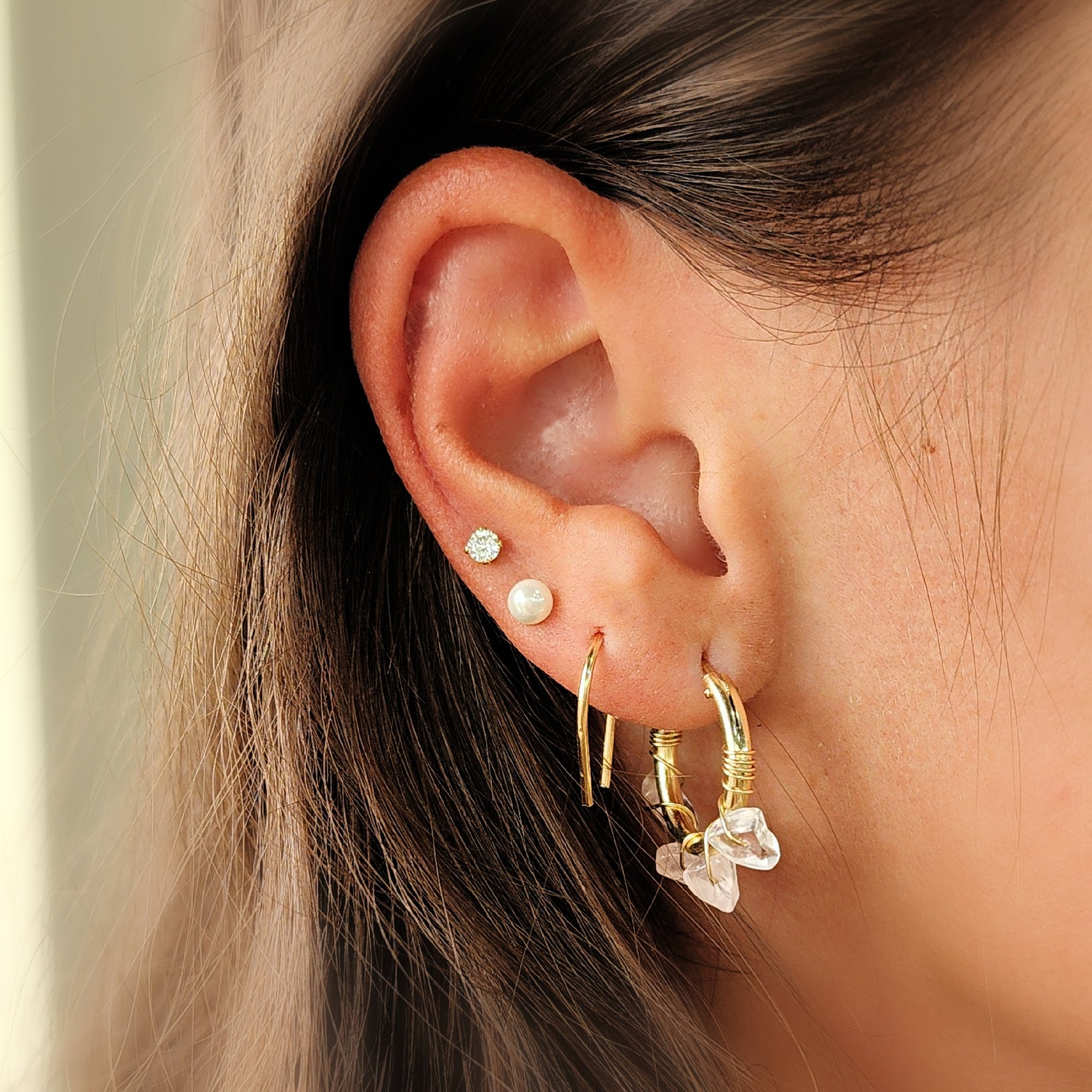 Gold U-shaped earrings stacked with other hoops on model’s ear