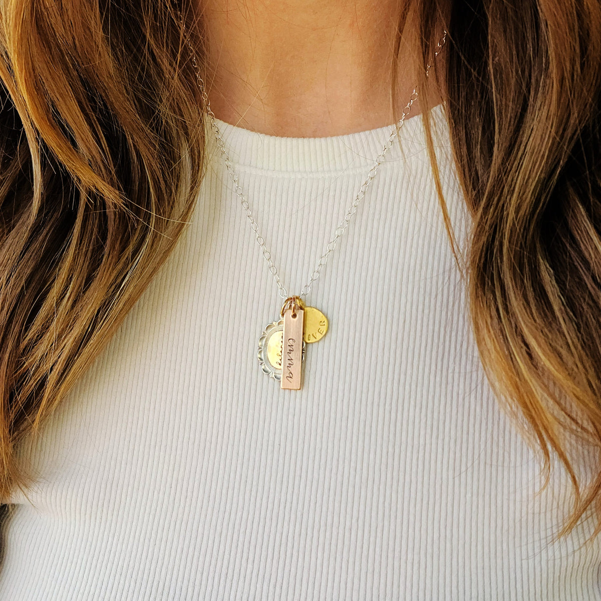 Necklace with gold pendants worn by a person with long hair, against a white background