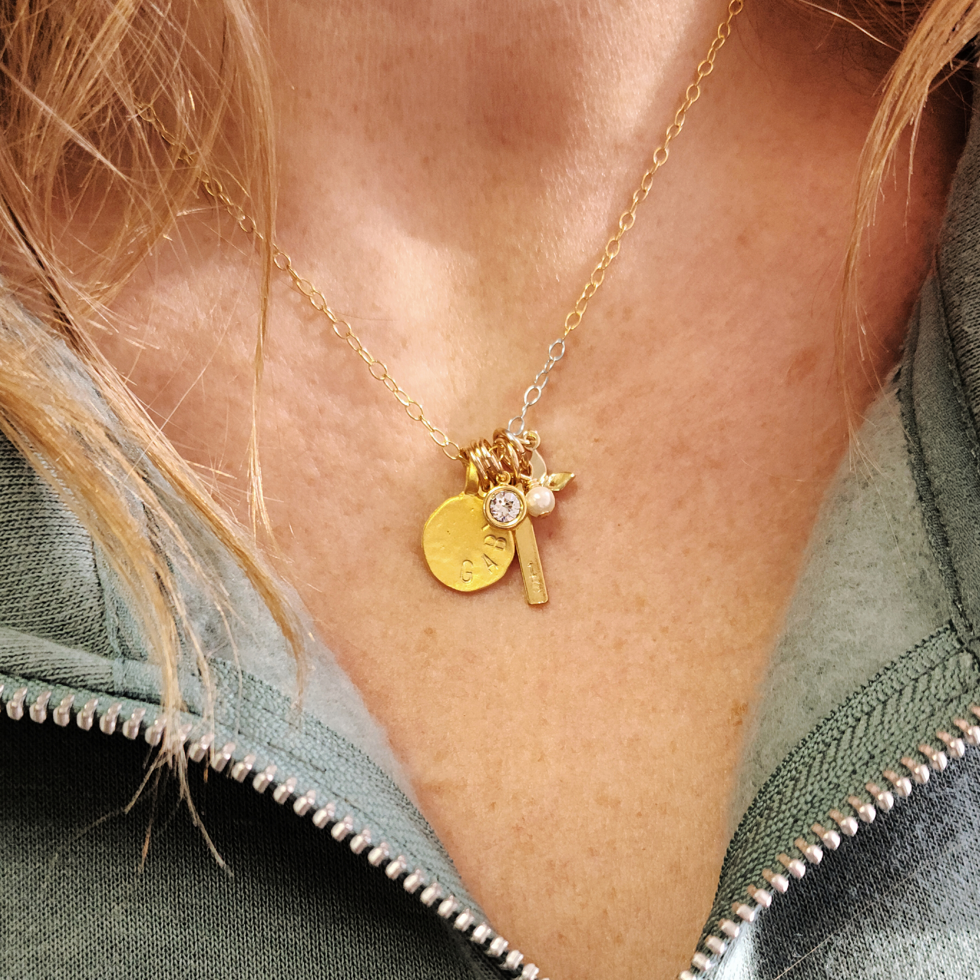 Gold necklace with charms on a person wearing a green jacket.