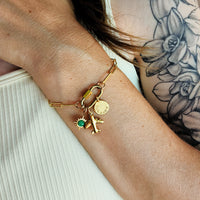 Gold bracelet with charms on a wrist against a neutral background