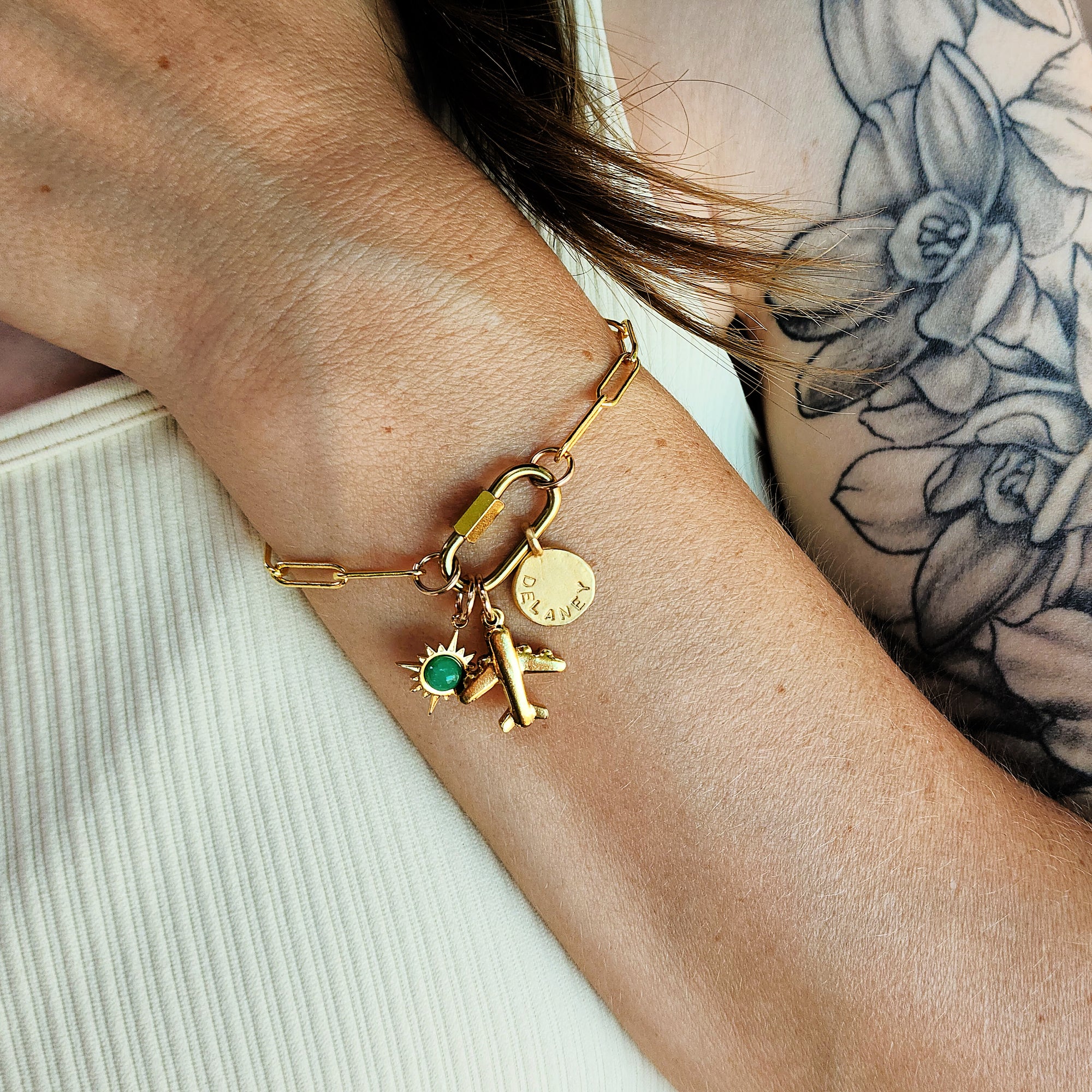 Gold bracelet with charms on a wrist against a neutral background