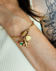 Gold bracelet with charms on a wrist against a neutral background