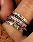 A hand wearing multiple gold-colored stacking rings with different designs, including personalized names.