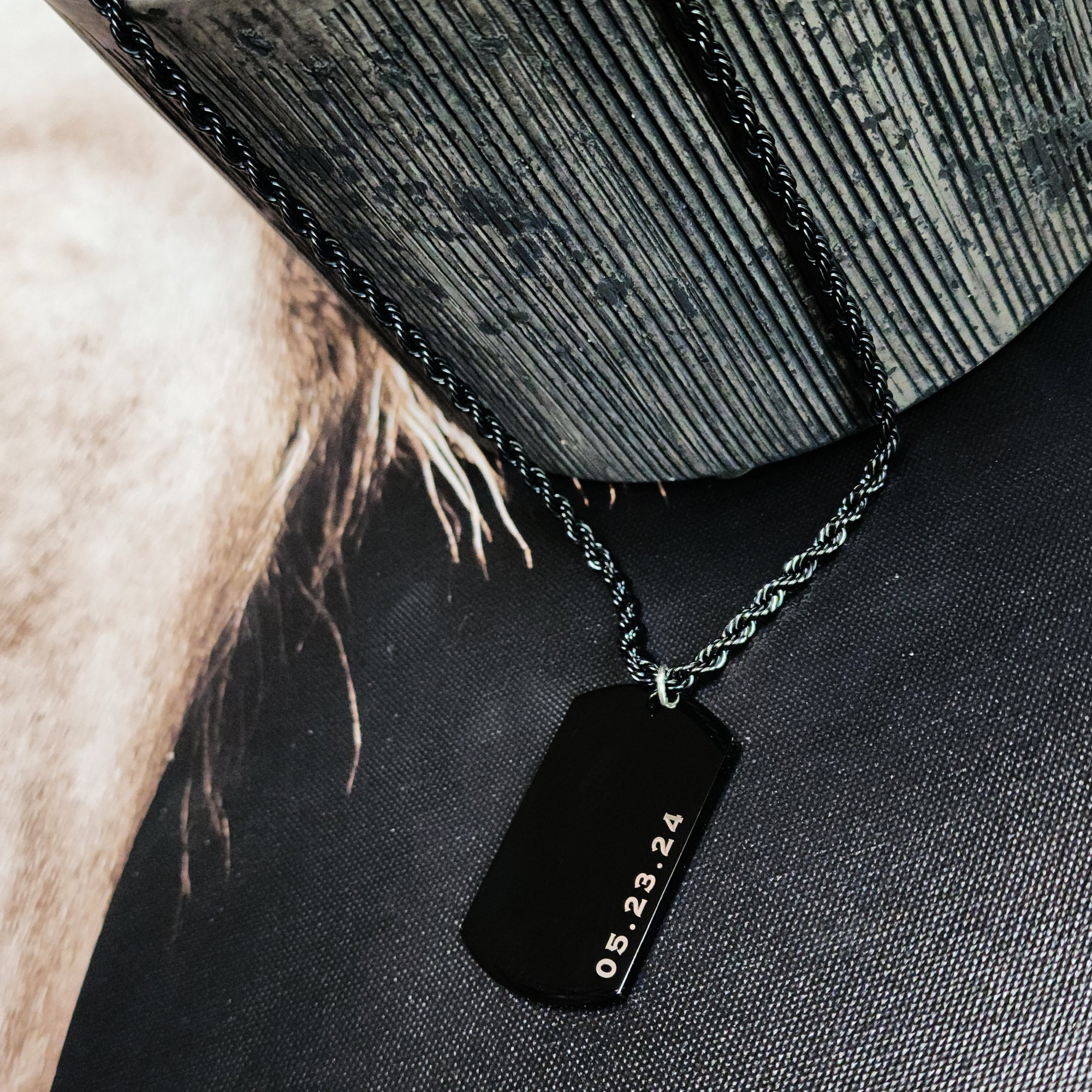 Black dog tag necklace with engraved date on a textured surface
