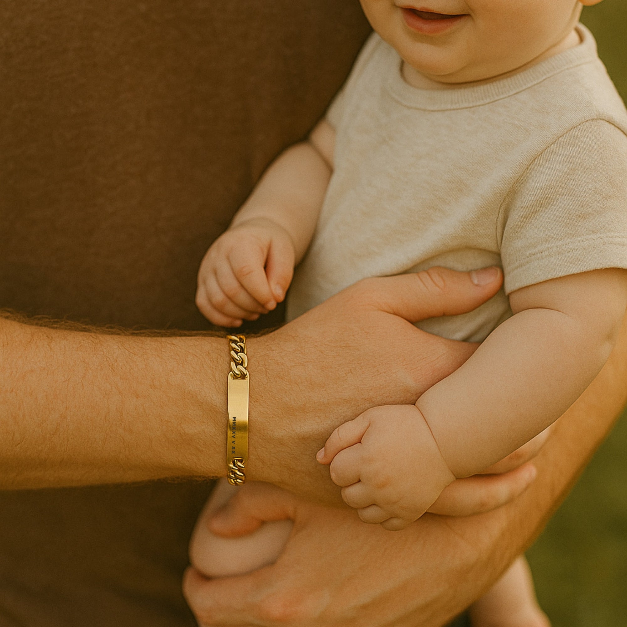 Person holding a baby with a gold bracelet on their wrist, set against a blurred natural background.