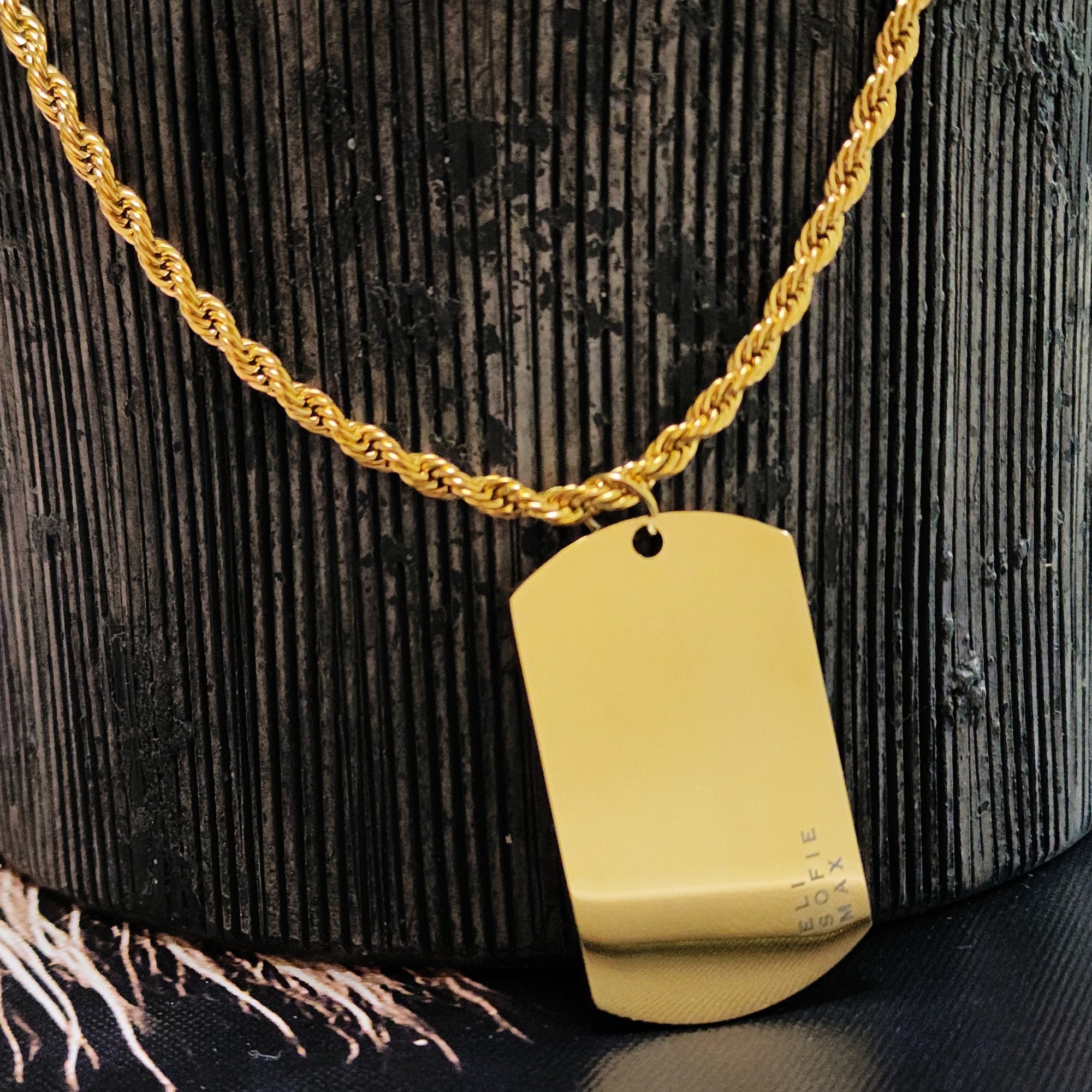 Gold necklace with a dog tag on a textured black surface
