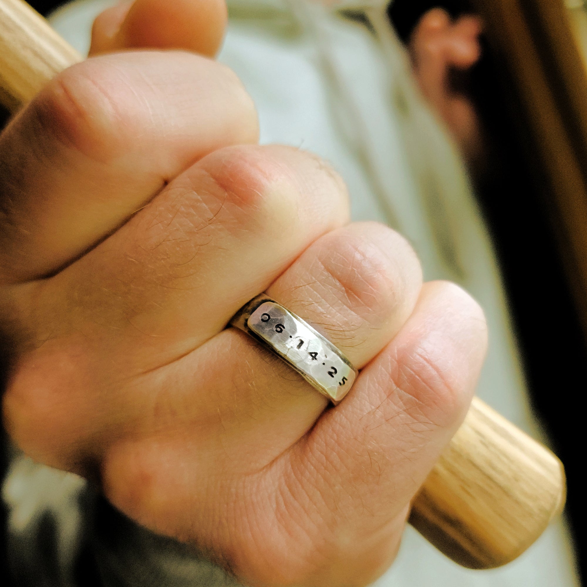 Hand wearing a silver ring with engraved numbers, holding a wooden object.