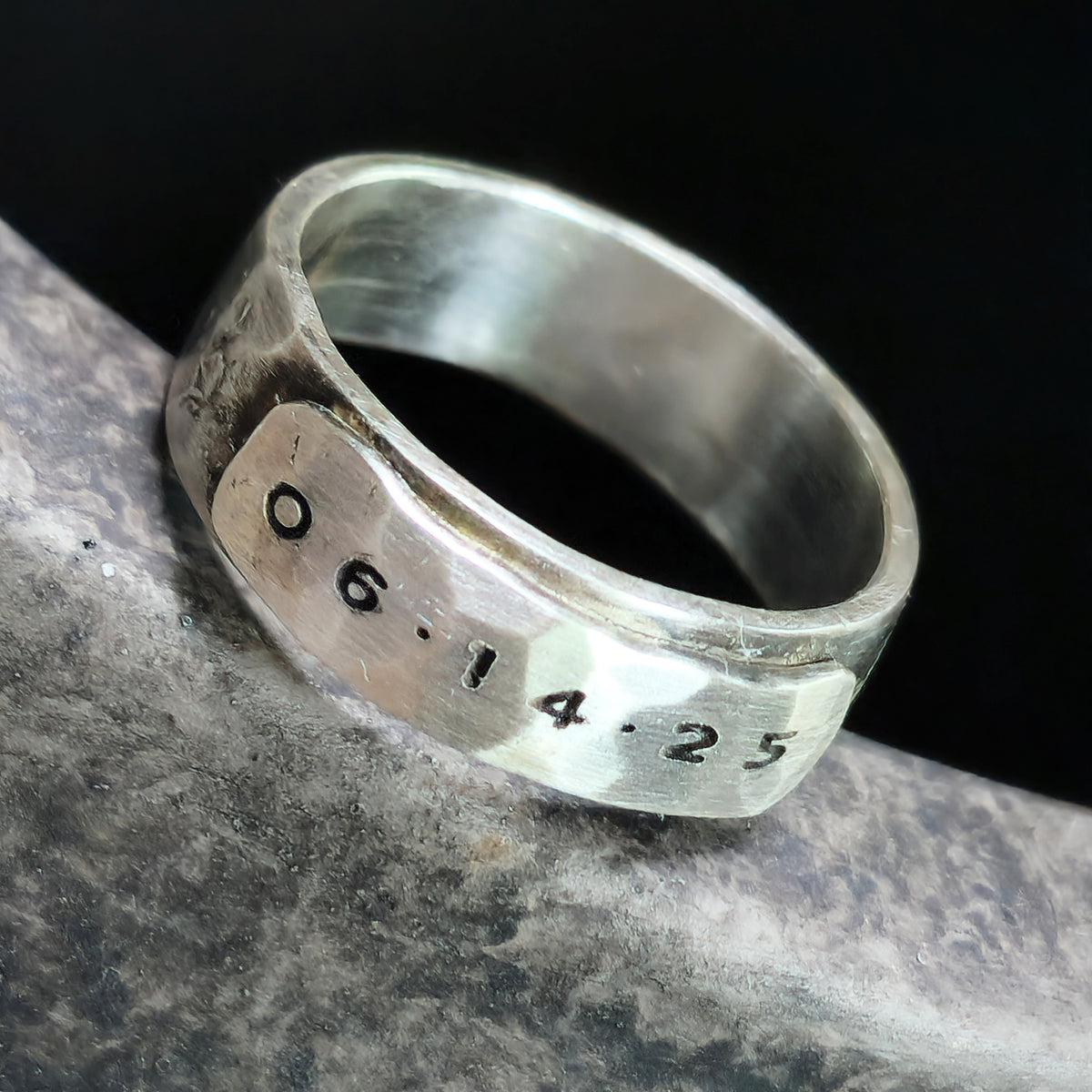 Silver ring with engraved date on a dark background