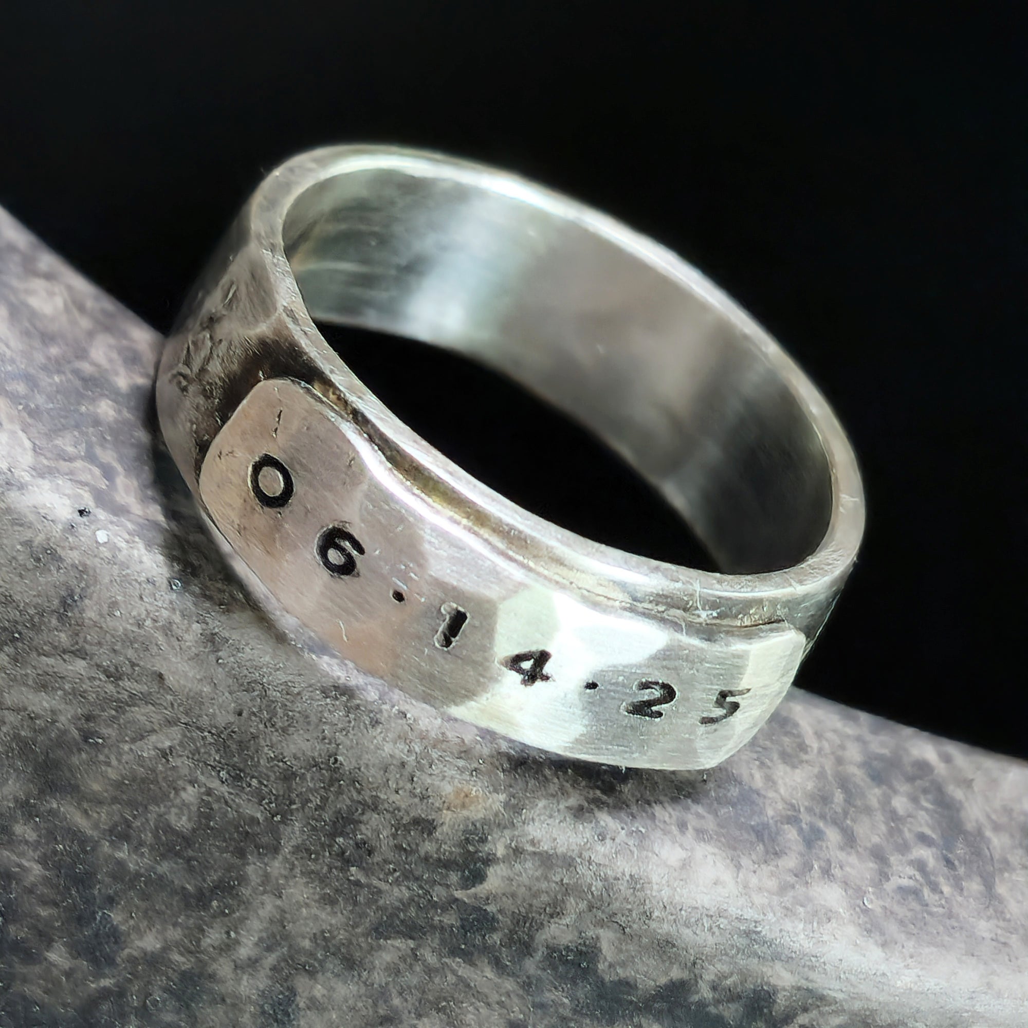 Silver ring with engraved date on a dark background