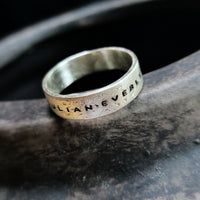 Silver ring with engraved text on a dark stone surface