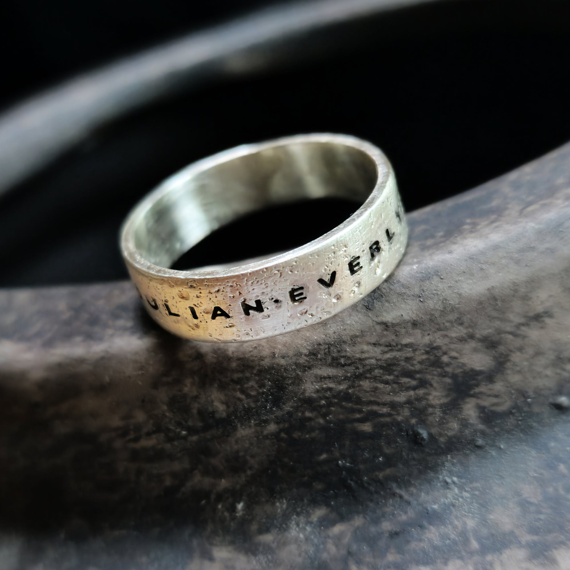 Silver ring with engraved text on a dark stone surface