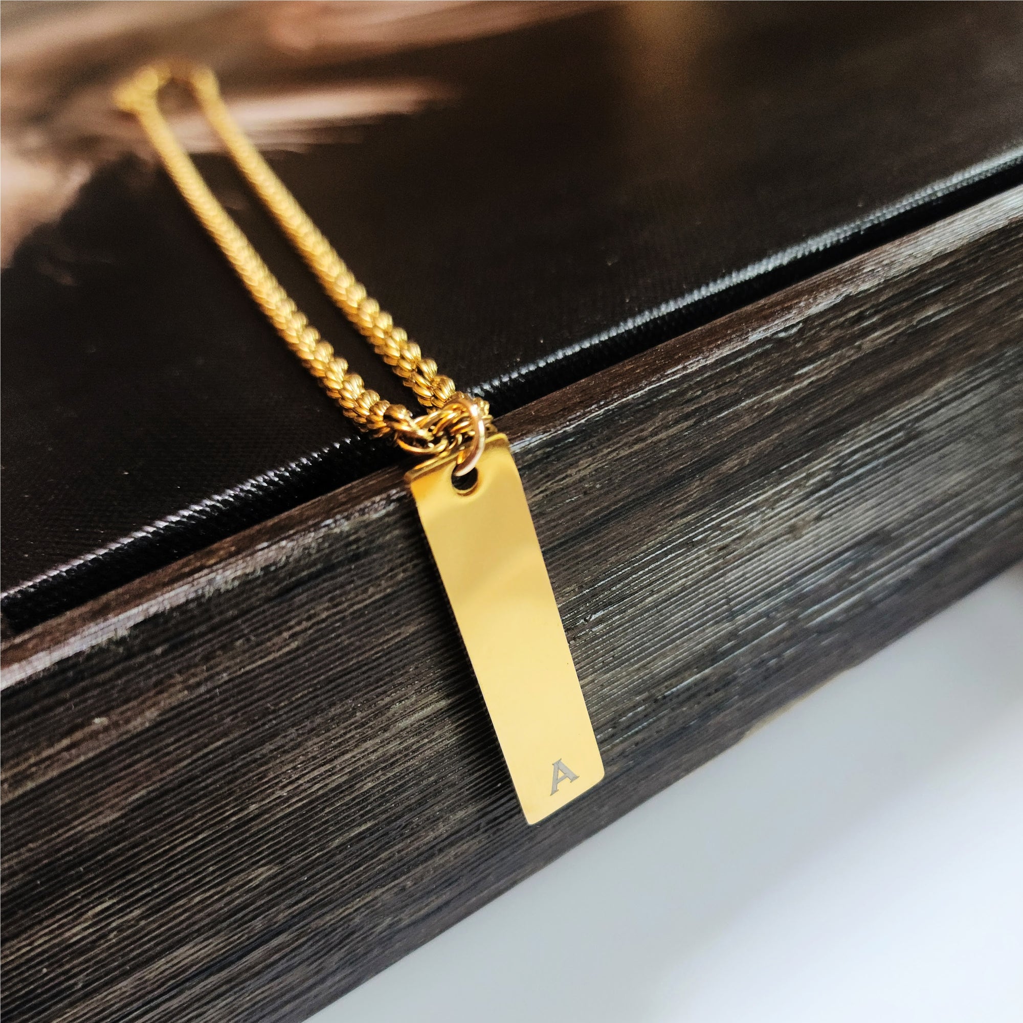 Gold necklace with a rectangular pendant on a wooden surface