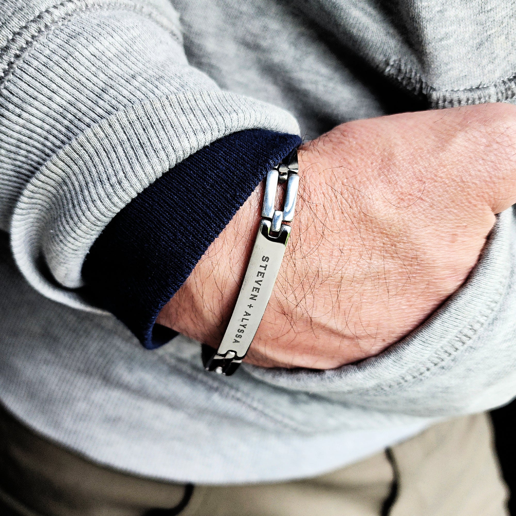 Close-up of a person wearing a silver bracelet with brand engraving.