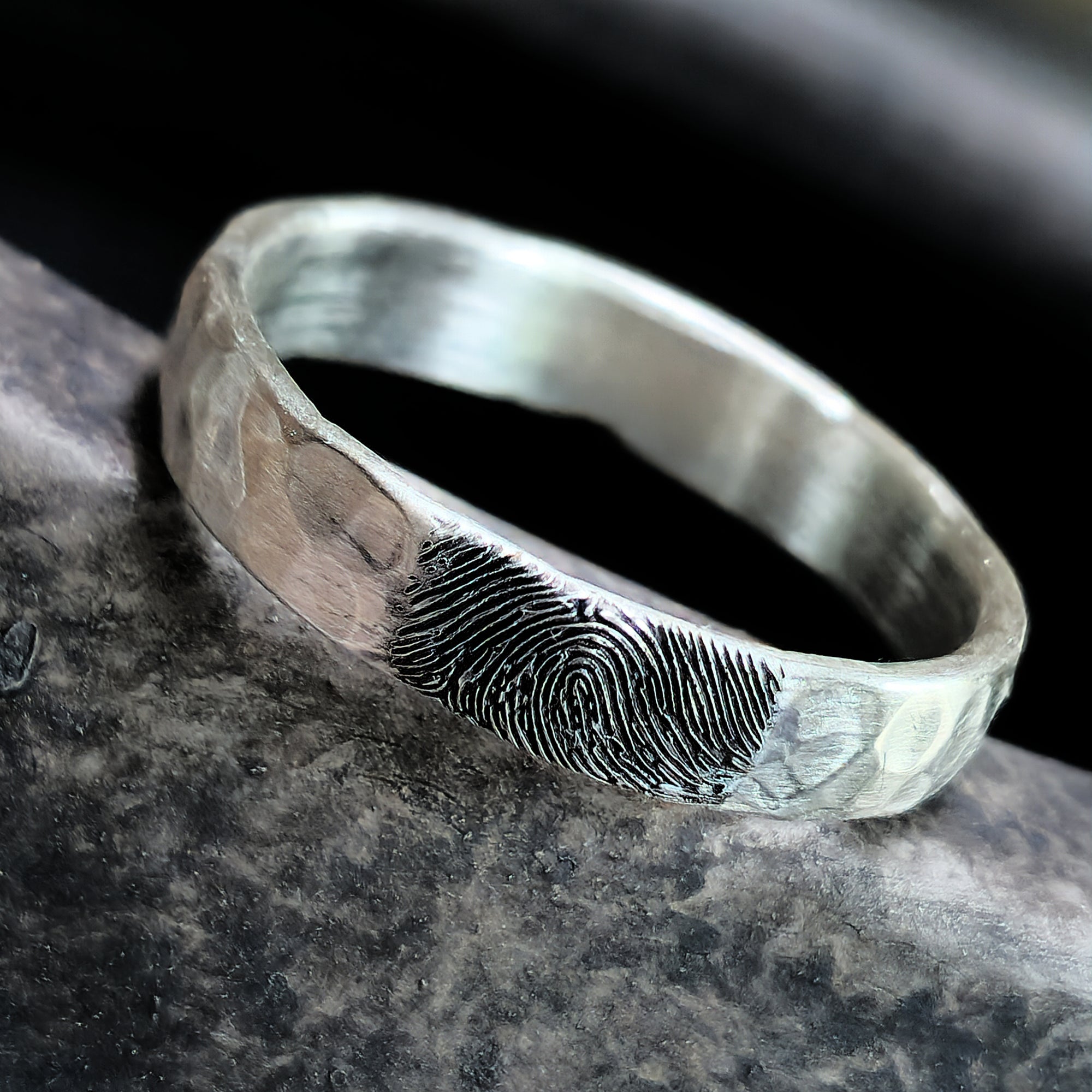 Silver ring with fingerprint engraving on a dark stone surface