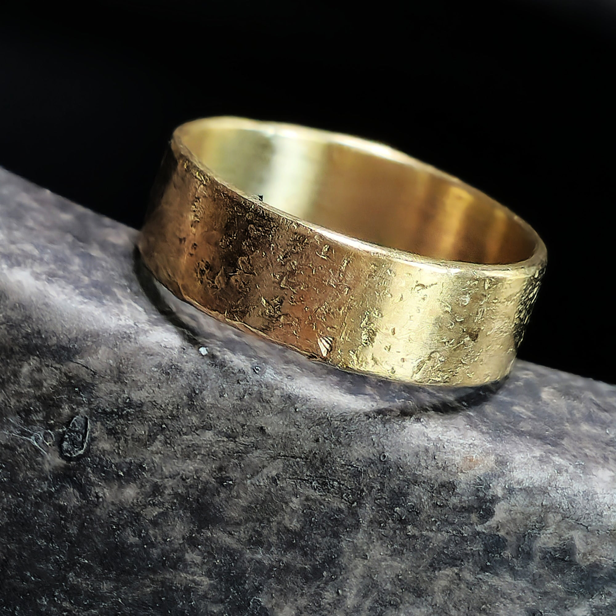 Gold ring with textured surface on a dark stone background