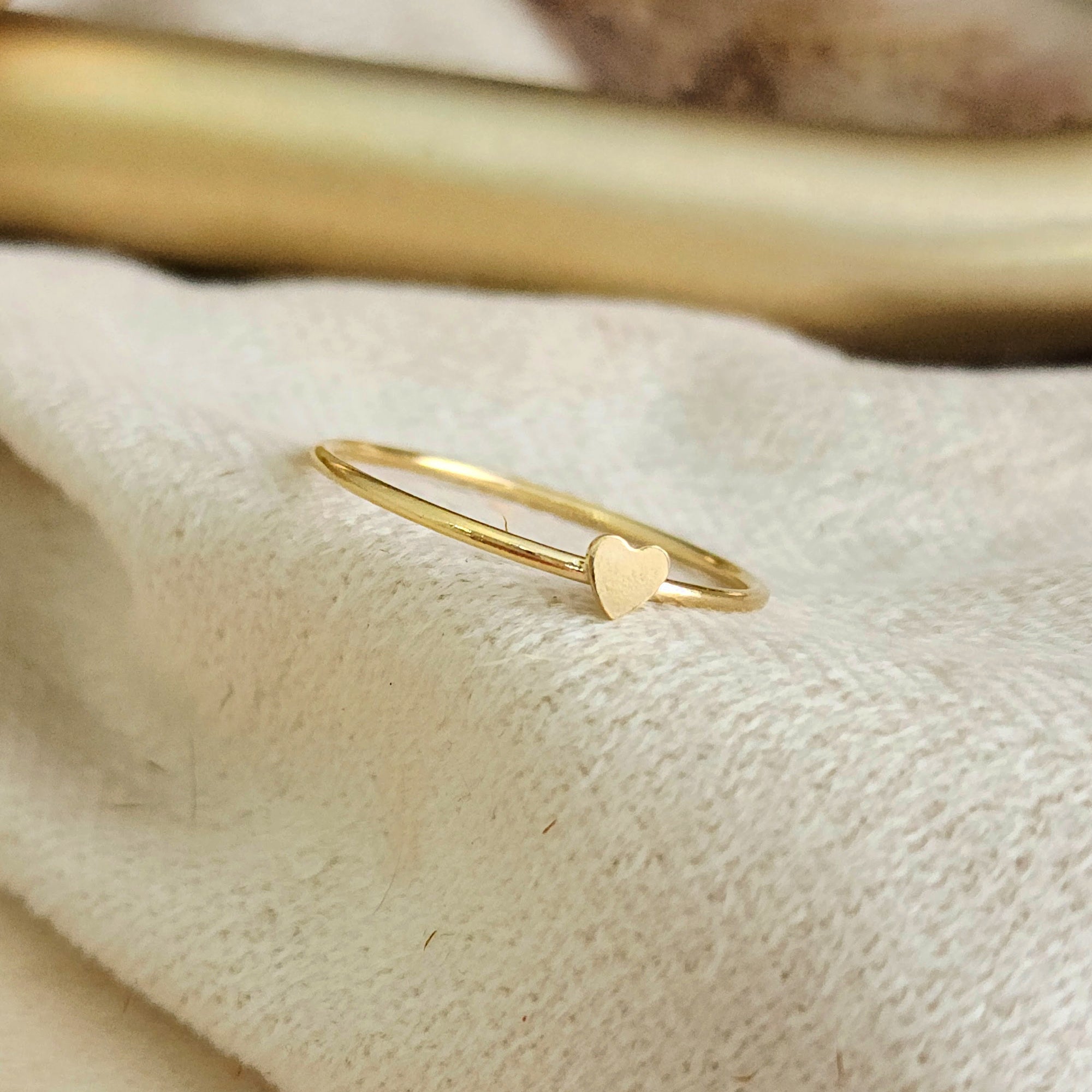 A gold-colored mini heart ring placed on a white fabric surface.