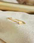 A gold-colored mini heart ring placed on a white fabric surface.