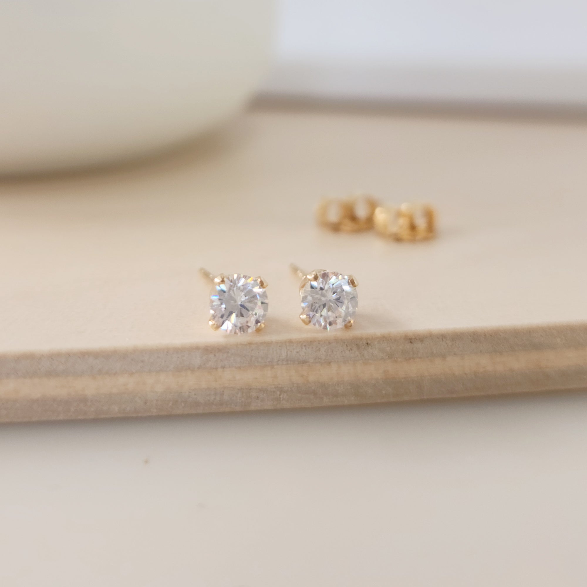 A pair of clear cubic zirconia stud earrings in gold settings, displayed on a wooden surface.