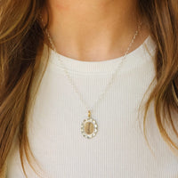 Close-up of a gold necklace with an oval pendant worn by a person against a white background