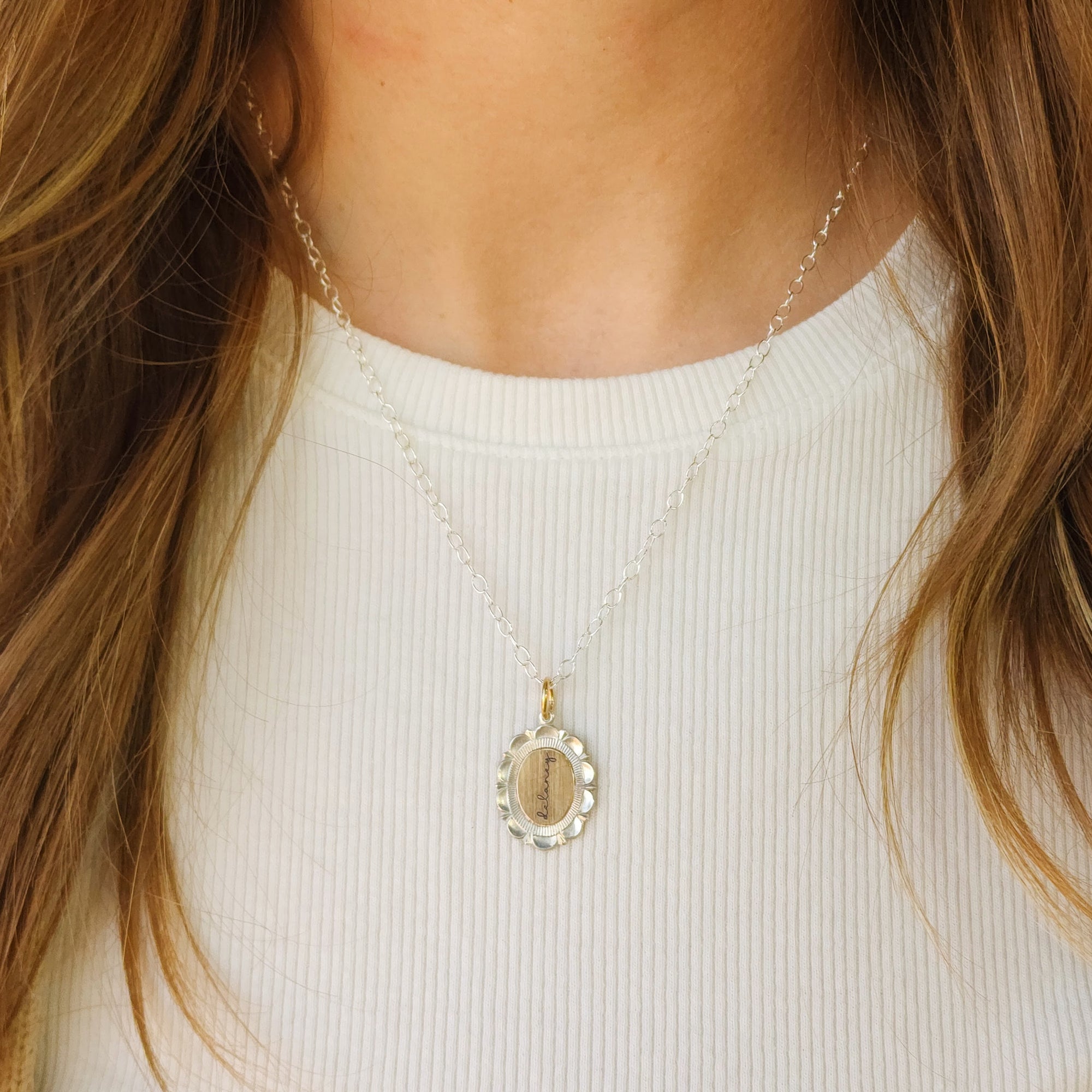 Close-up of a gold necklace with an oval pendant worn by a person against a white background