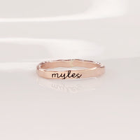 A gold-colored thin ring with cursive script engraving on a white background.