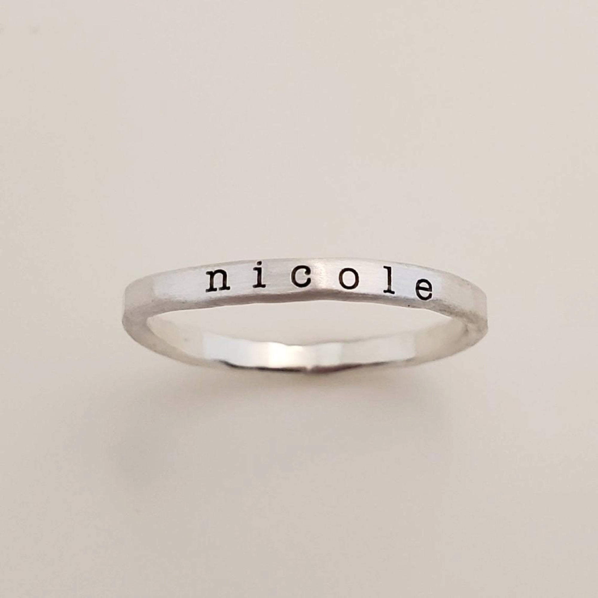A gold-colored ring with the name &#39;nicole&#39; engraved in a typewriter-style font.