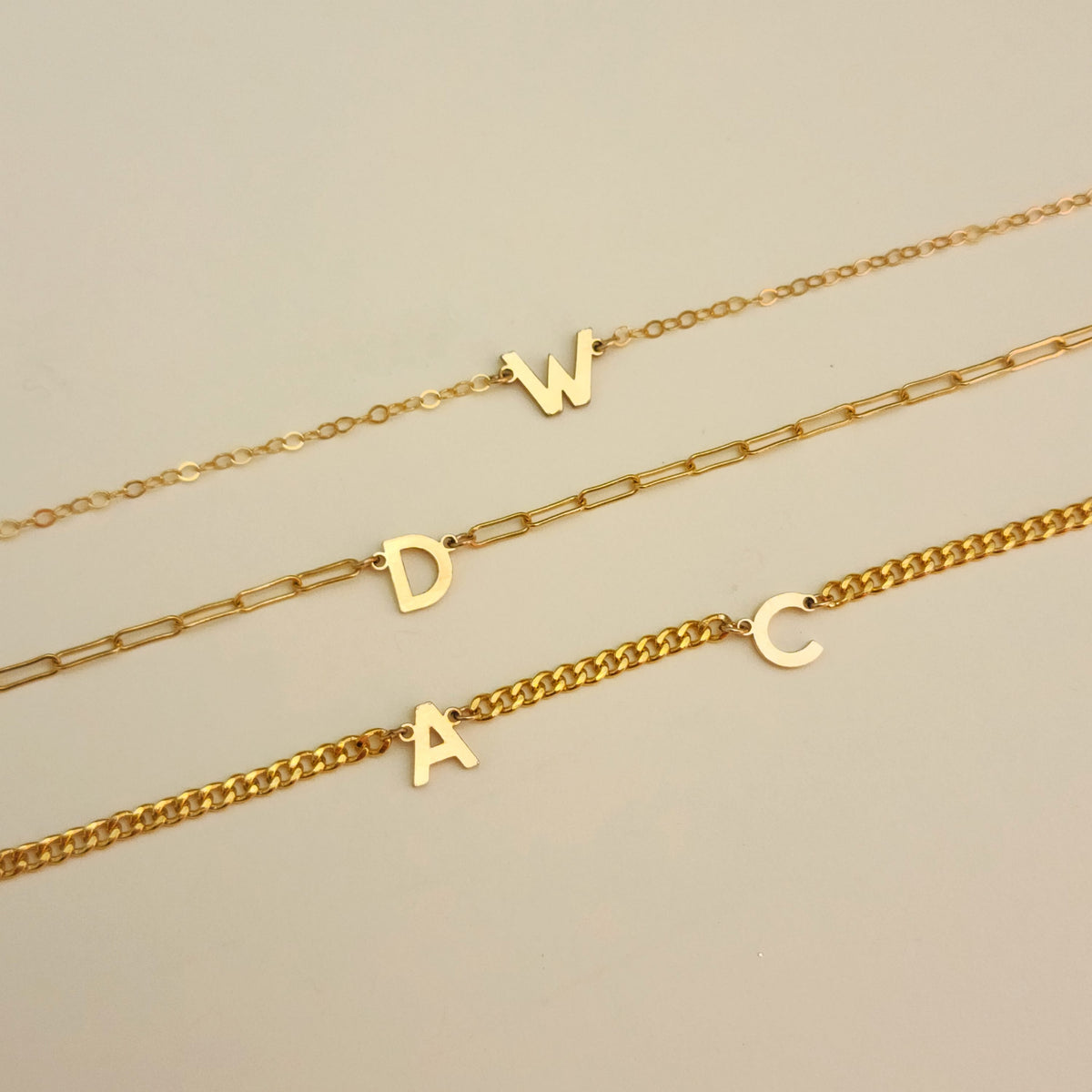 Three gold necklaces with letter pendants on a beige background