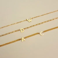 Three gold necklaces with letter pendants on a beige background