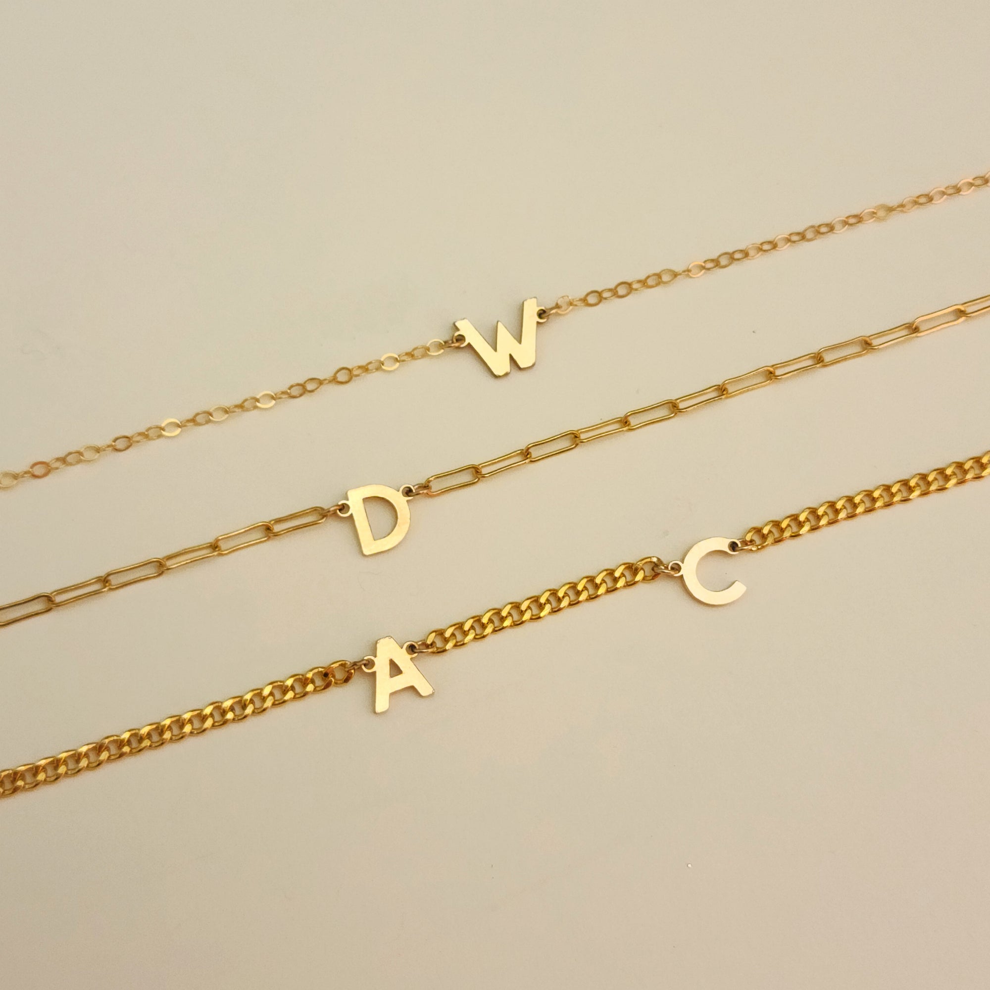 Three gold necklaces with letter pendants on a beige background