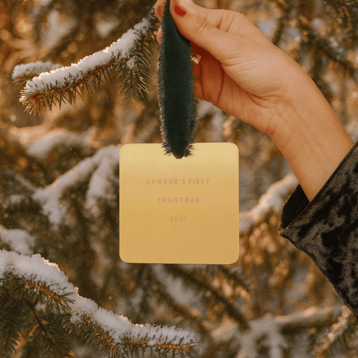 Hand holding a gold card with 'Dawson's First Christmas 2021' text against a snowy tree background.