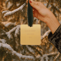 Hand holding a gold card with 'Dawson's First Christmas 2021' text against a snowy tree background.