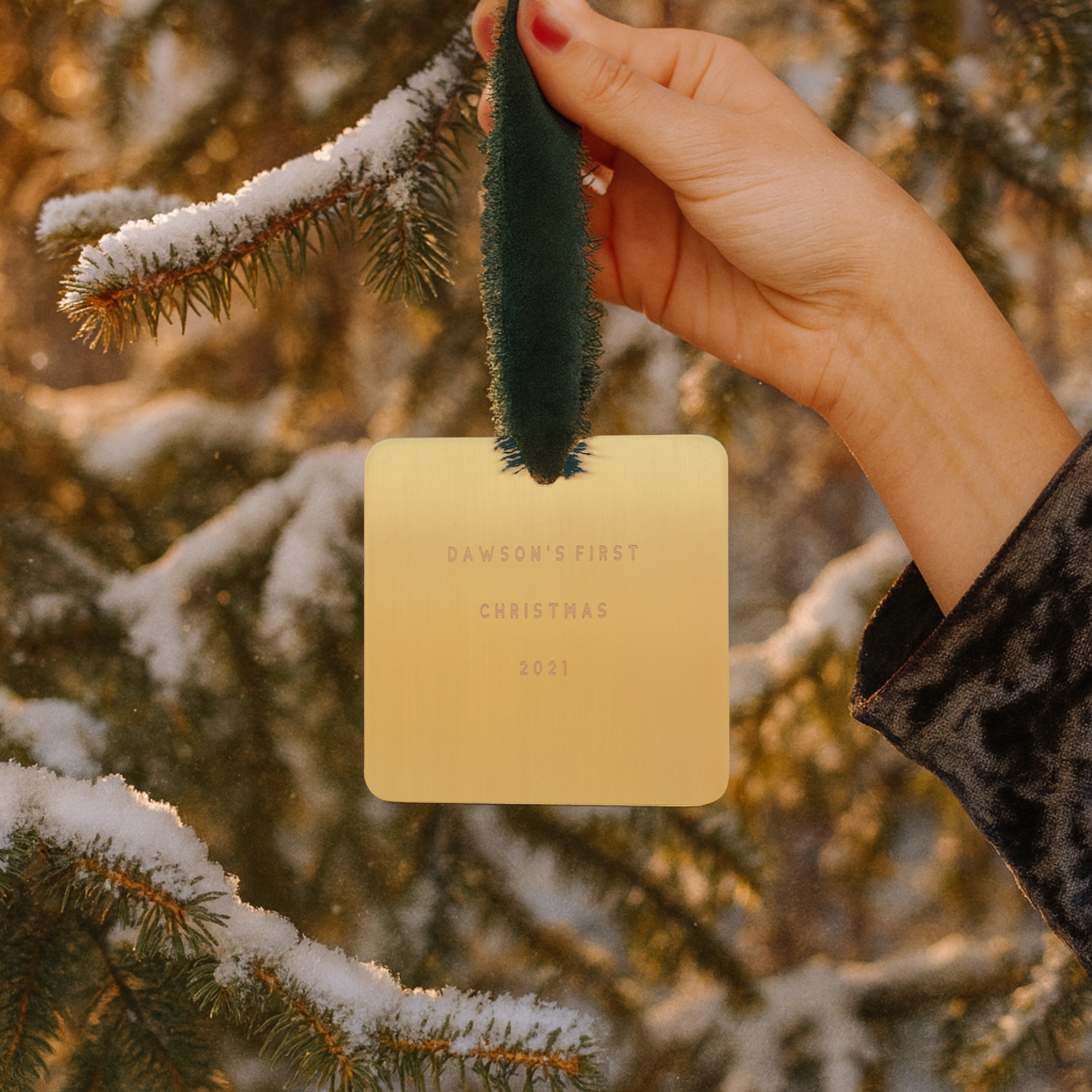 Hand holding a gold card with 'Dawson's First Christmas 2021' text against a snowy tree background.