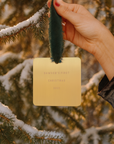 Hand holding a gold card with 'Dawson's First Christmas 2021' text against a snowy tree background.