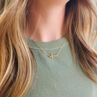 14K gold-filled personalized cross necklace layered with second gold necklace on model wearing green shirt
