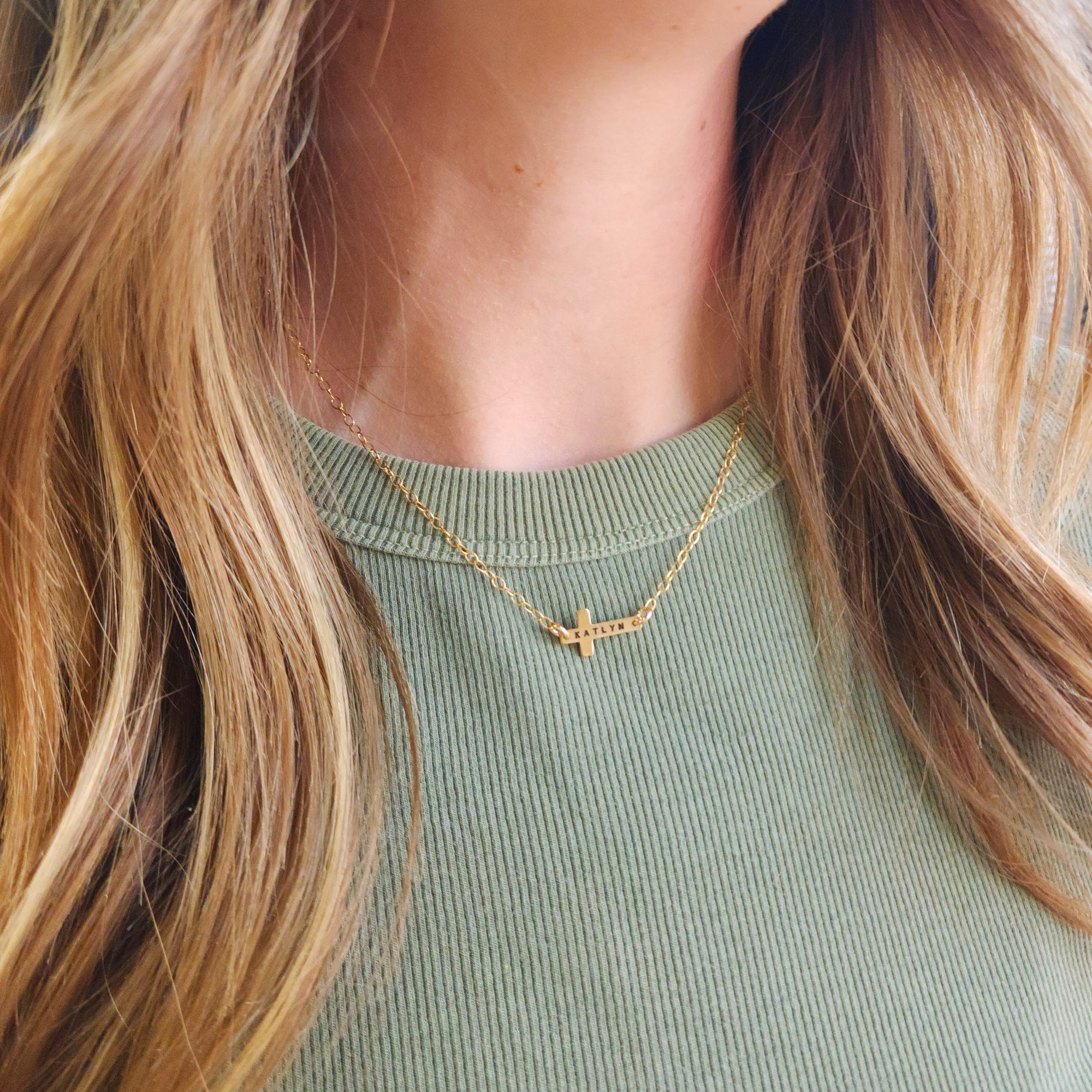 14K gold-filled personalized cross necklace layered with second gold necklace on model wearing green shirt