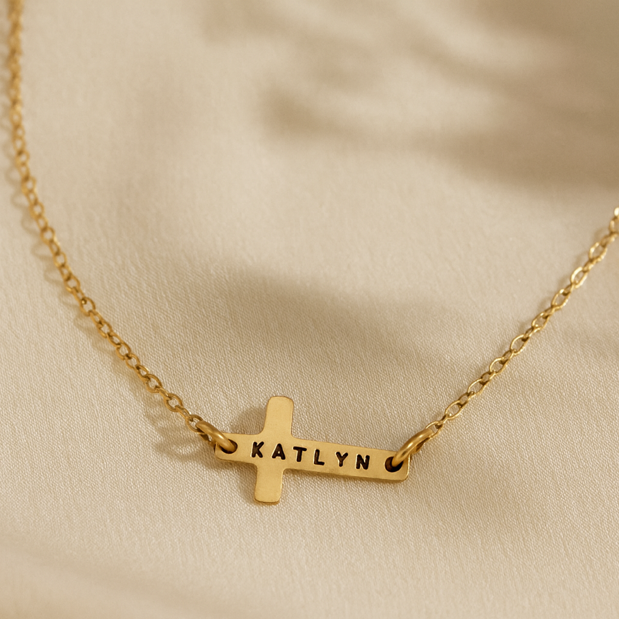 14K gold-filled personalized cross necklace engraved with the name Katlyn on cream background