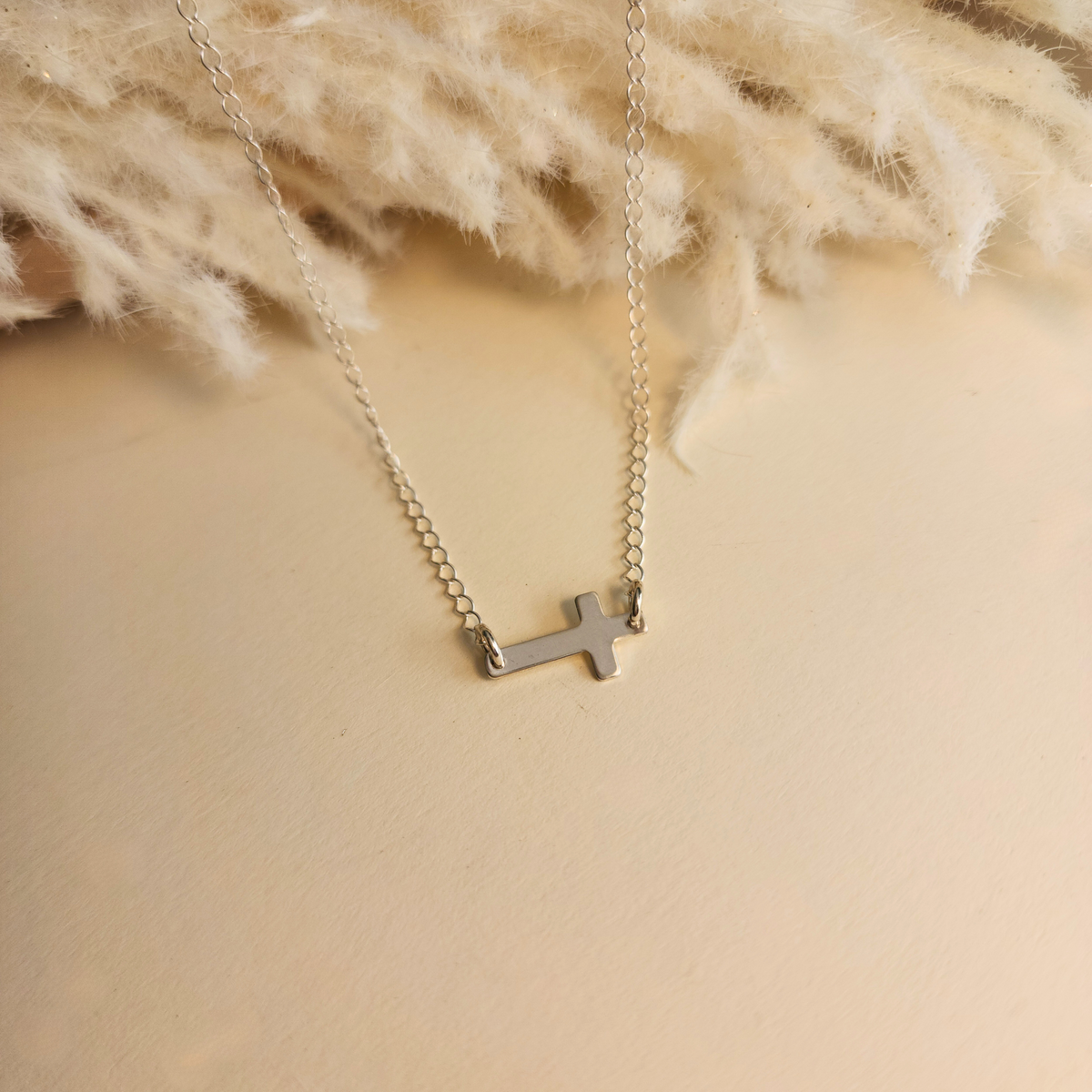 Sterling silver personalized cross necklace with blank engraving displayed on cream knit fabric
