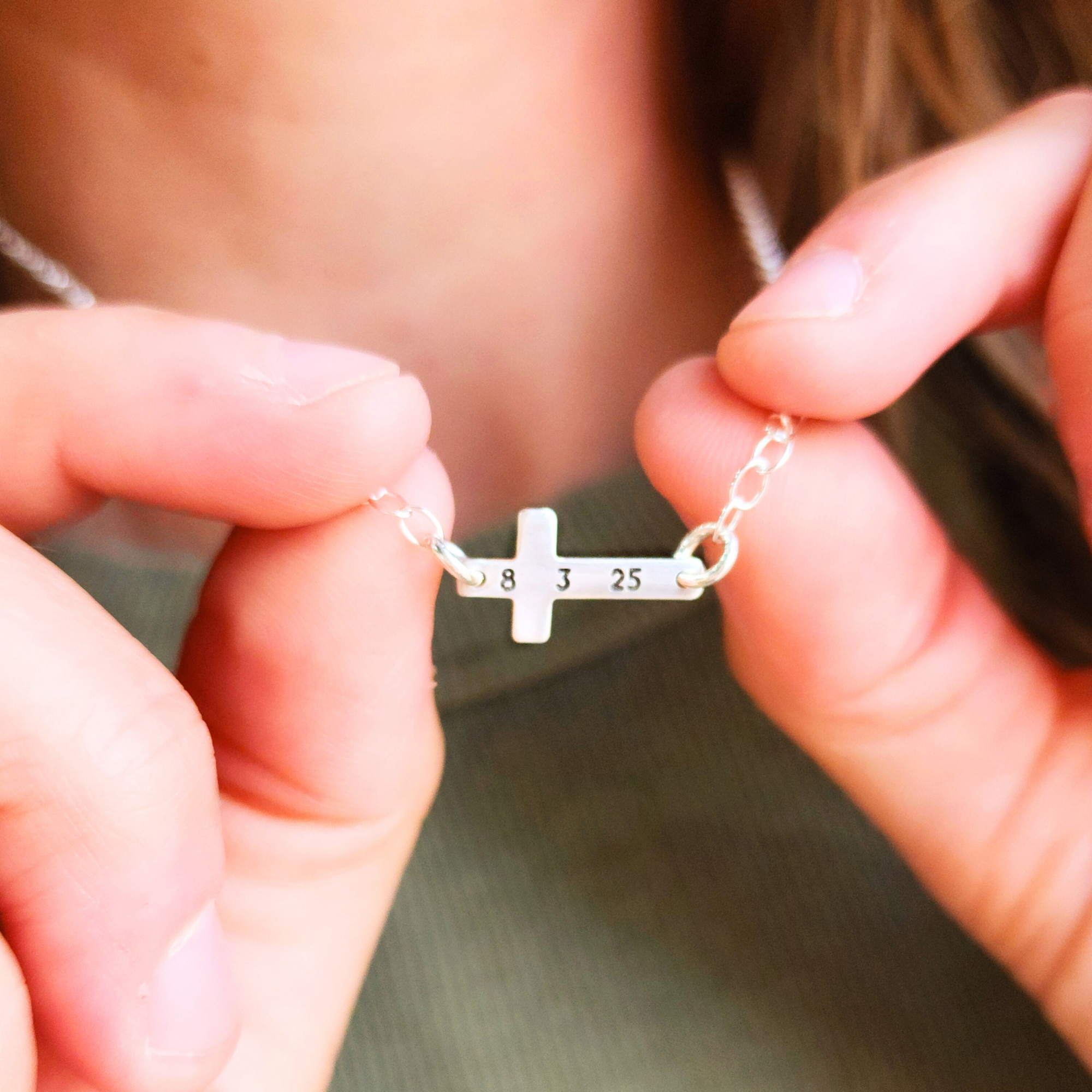 Close-up of sterling silver personalized cross necklace engraved with date 8 3 25 held in hands
