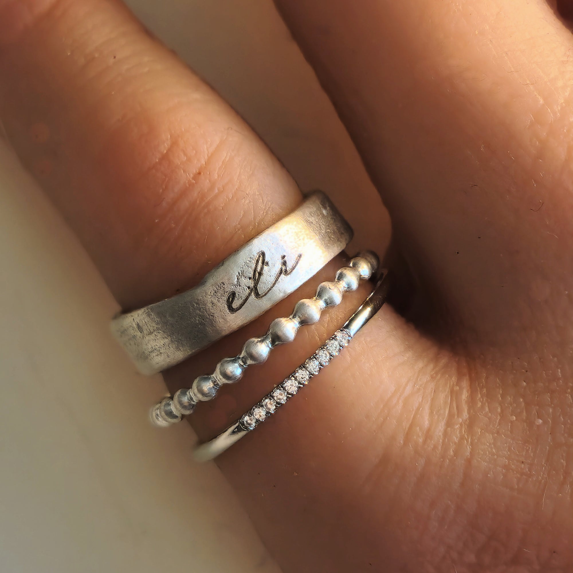 Close-up of a hand wearing multiple silver rings with different designs.