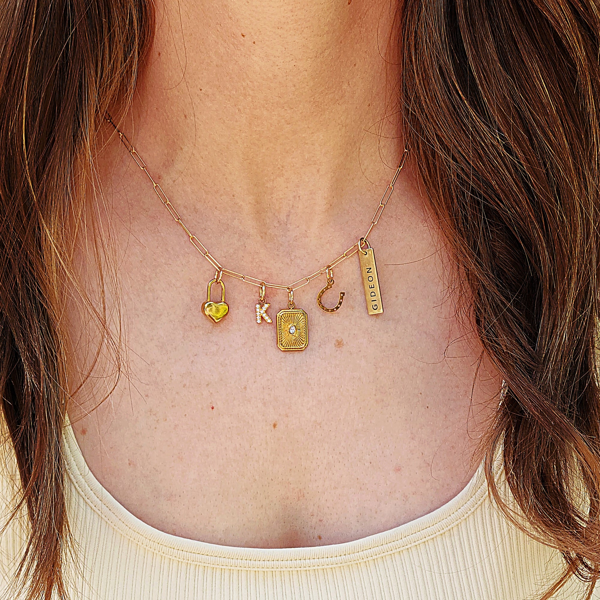 Gold necklace with various charms on a person wearing a beige top.