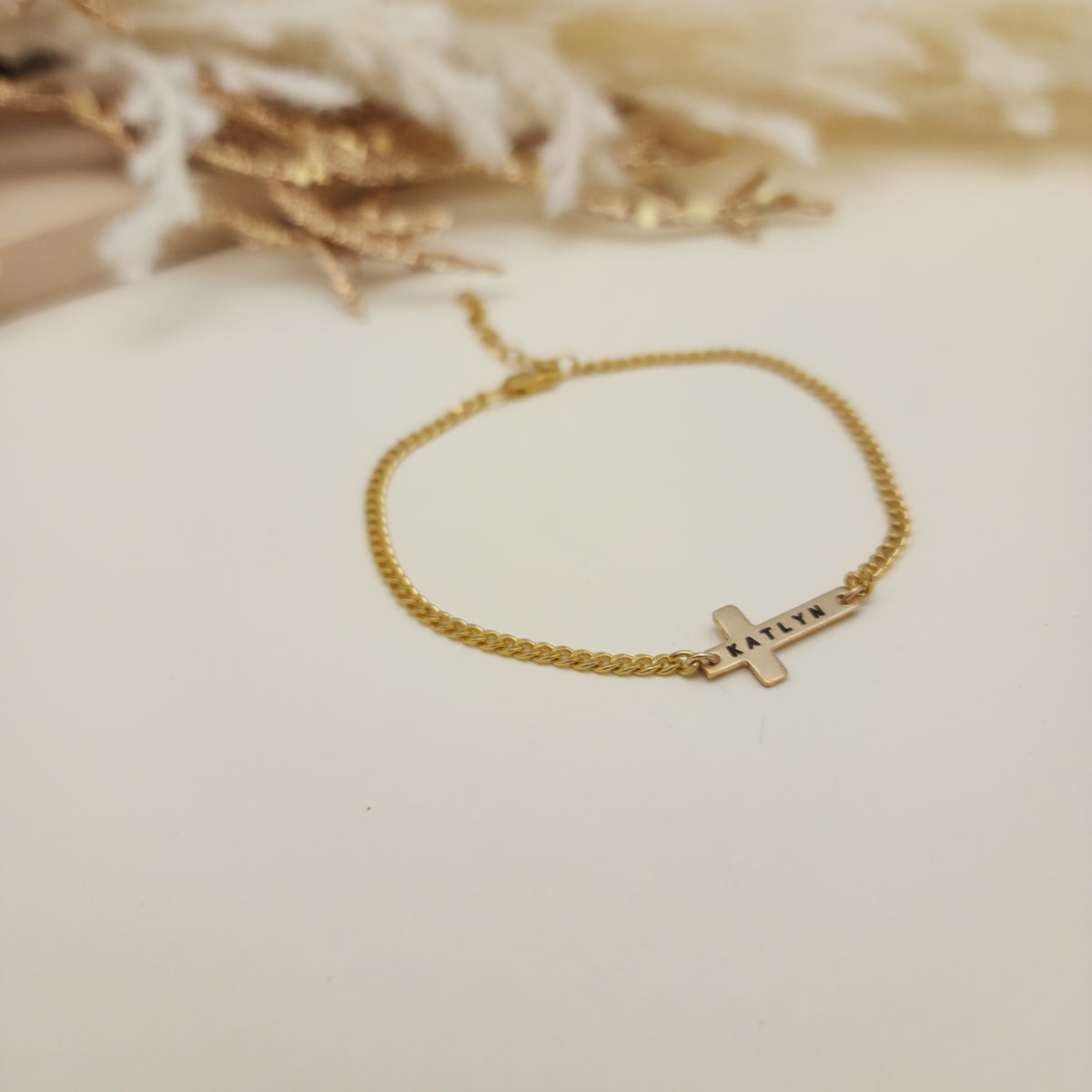 Gold bracelet with a cross charm on a soft beige background