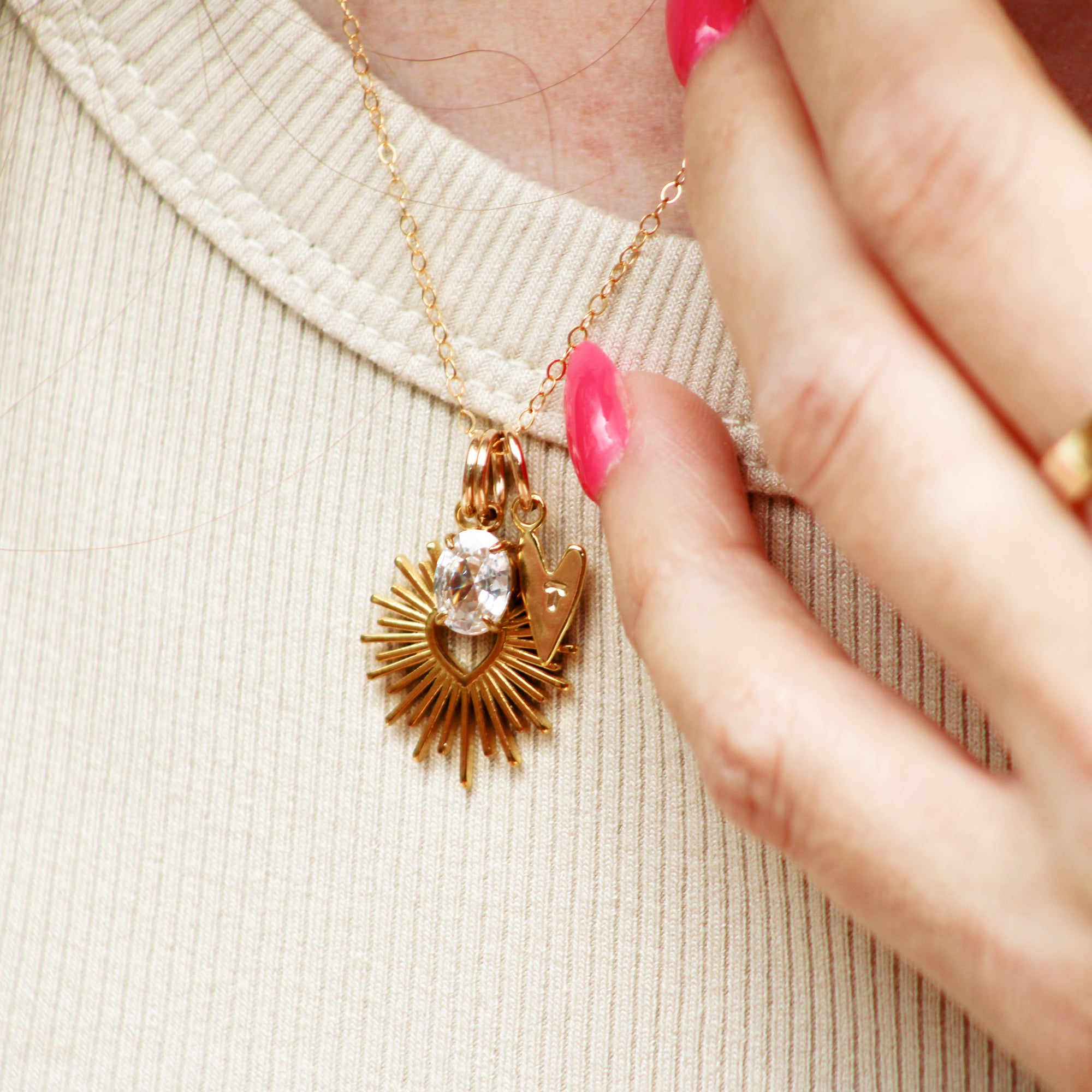 Gold necklace with a pendant held by a hand on a beige fabric background