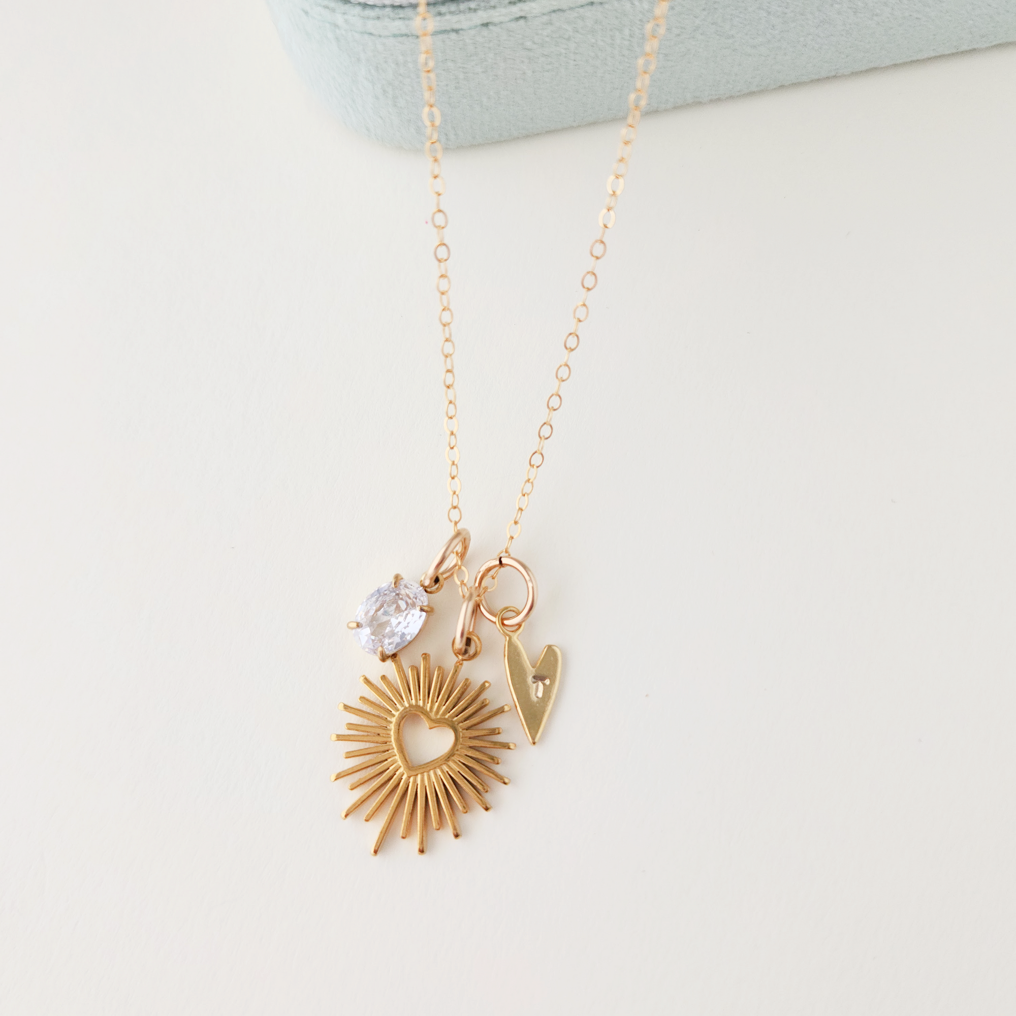 Gold necklace with sunburst pendant and heart-shaped charm on a light gray background